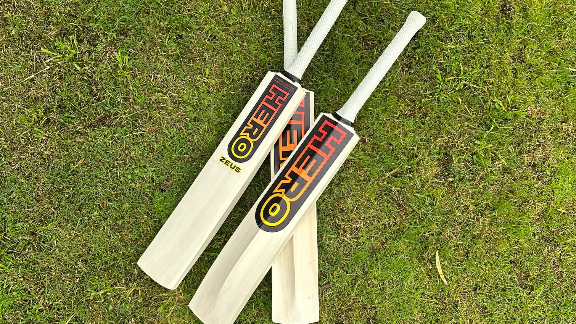 Two cricket bats with visible branding on a grassy background