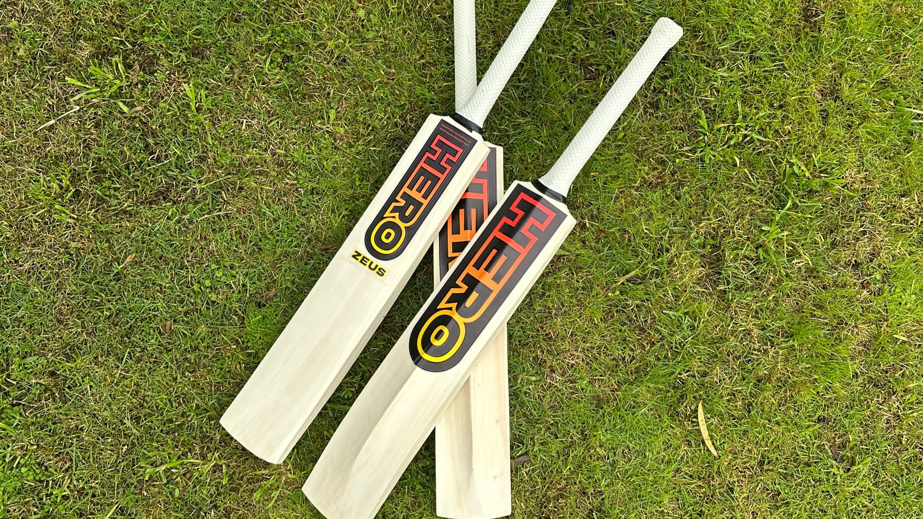 Two cricket bats with visible branding on a grassy background
